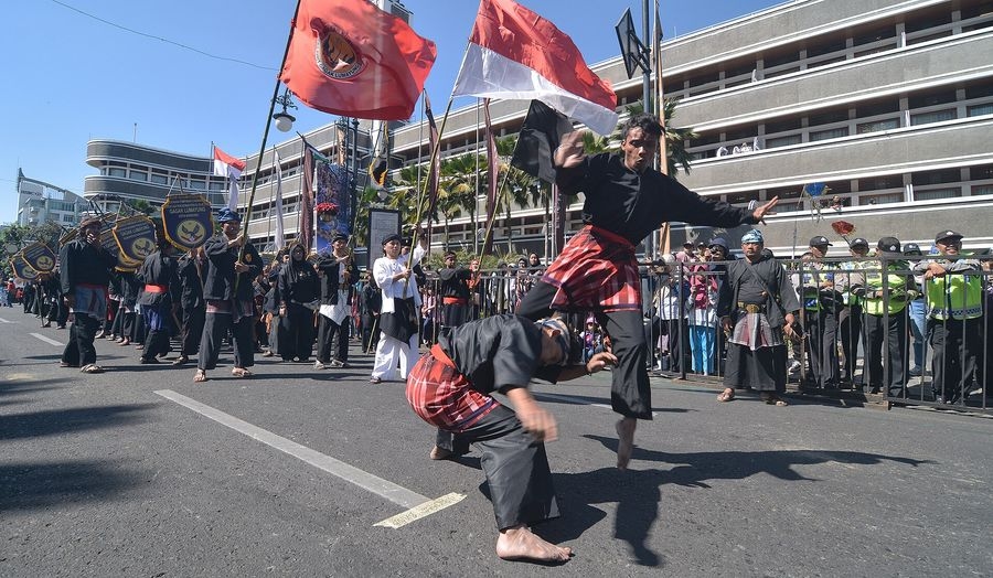 Deux pratiquants en tenue traditionnelle noire et sarong rouge exécutant une démonstration de pencak silat lors d'un défilé de rue en Indonésie