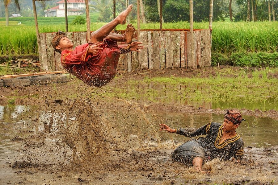 Démonstration de silek lanyah, silat traditionnel minangkabau pratiqué dans une rizière boueuse : un pratiquant saute au-dessus de son partenaire au sol