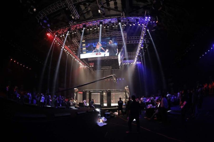 Salle plongée dans la pénombre, faisceaux lumineux et écran géant au-dessus de la cage lors d'un gala de MMA à Bahreïn
